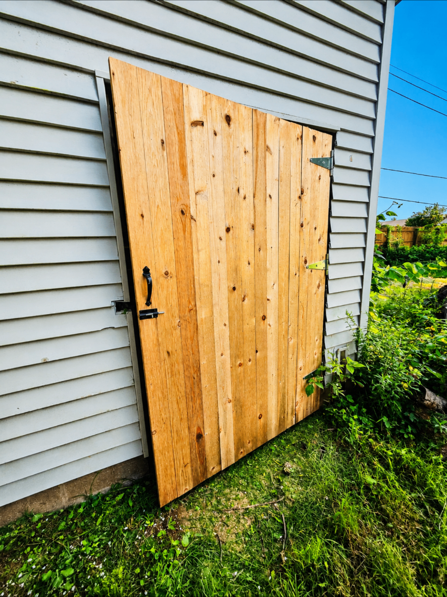 Rustic handmade wooden shed door installed beside a garden